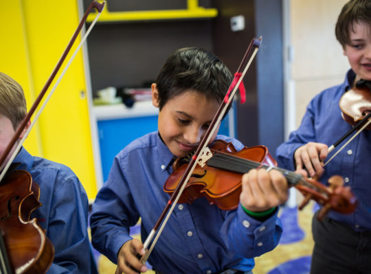A boy playing the violin in front of other boys.